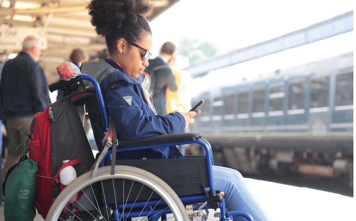 mixed race disabled young woman in wheelchair at station looking at phone