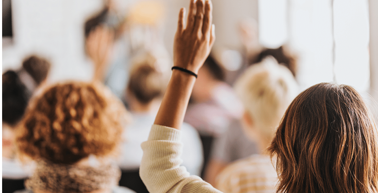 Rear view of casual businesswoman raising her arm to ask the question on education event in a board room.