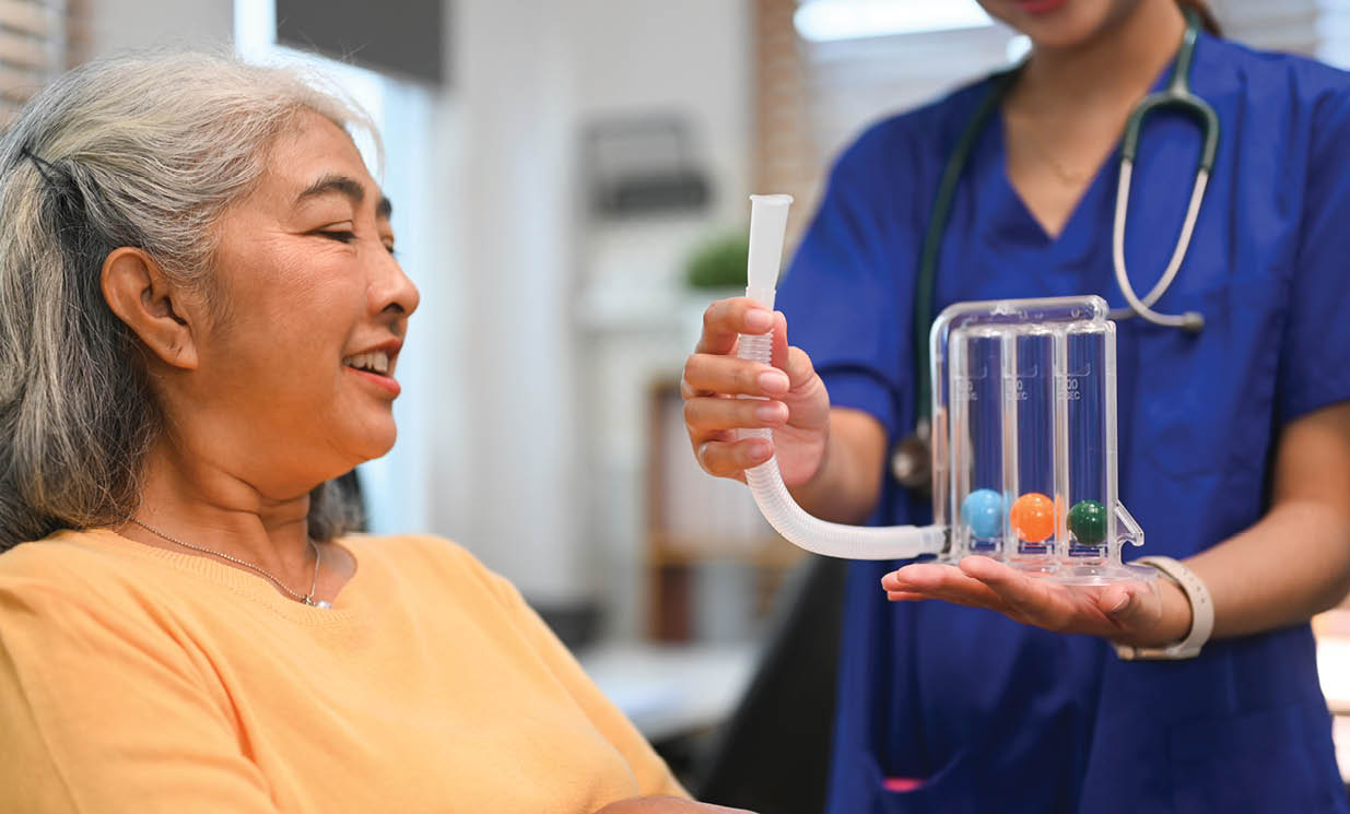 Physical therapist assisting mature woman with using a spirometer to improve the functioning of lungs.