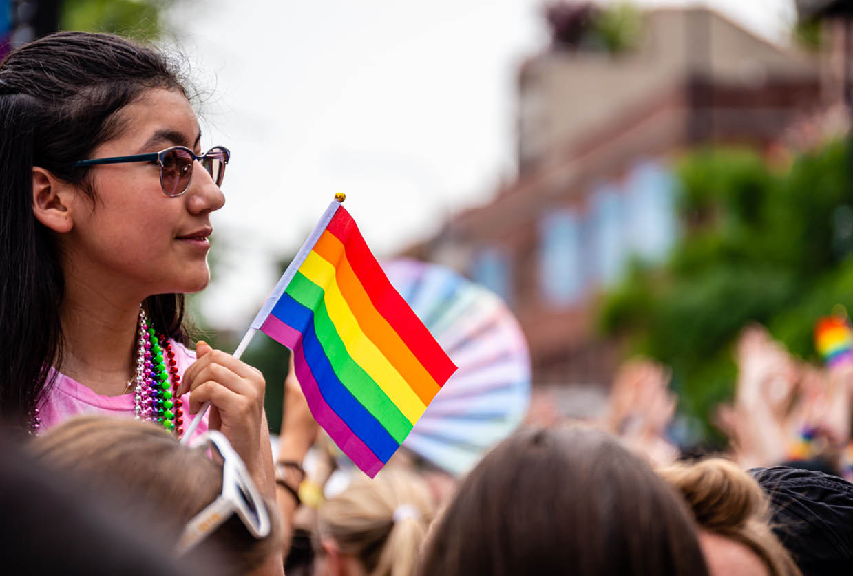 Lakeview, Chicago-June 30, 2019: A smiling young woman is watching the Gay Pride parade above the crowd while holding a rainbow flag.