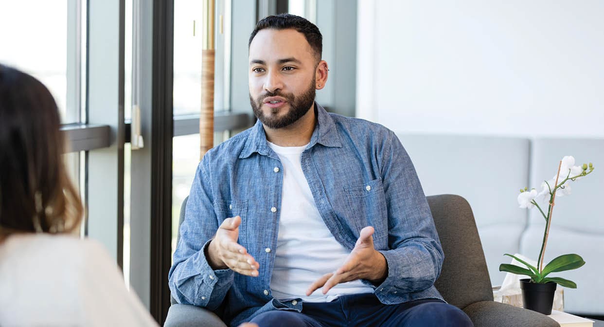 A young man gestures as he shares something during a therapy session.