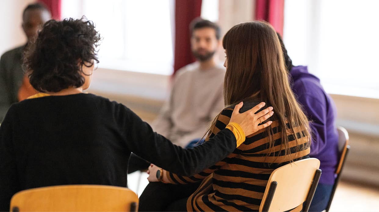 Supportive people consoling a distraught woman who is talking about her issues during group therapy meeting. Multi-ethnic group of adults attending a group therapy session.
