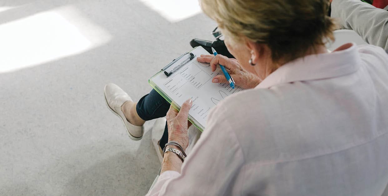 Senior woman patients sitting in waiting room filling out medical forms.