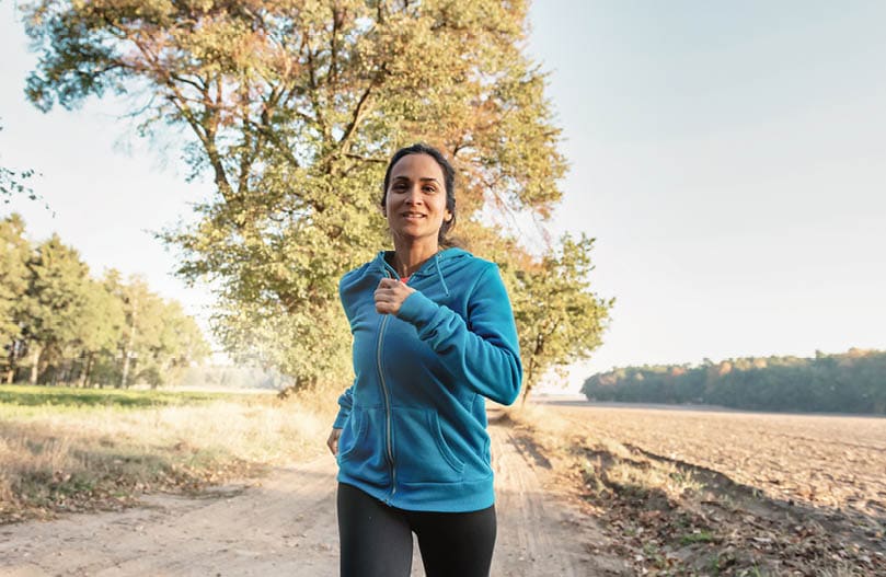 view on woman running in rural landscape in the morning sun, looking at camera