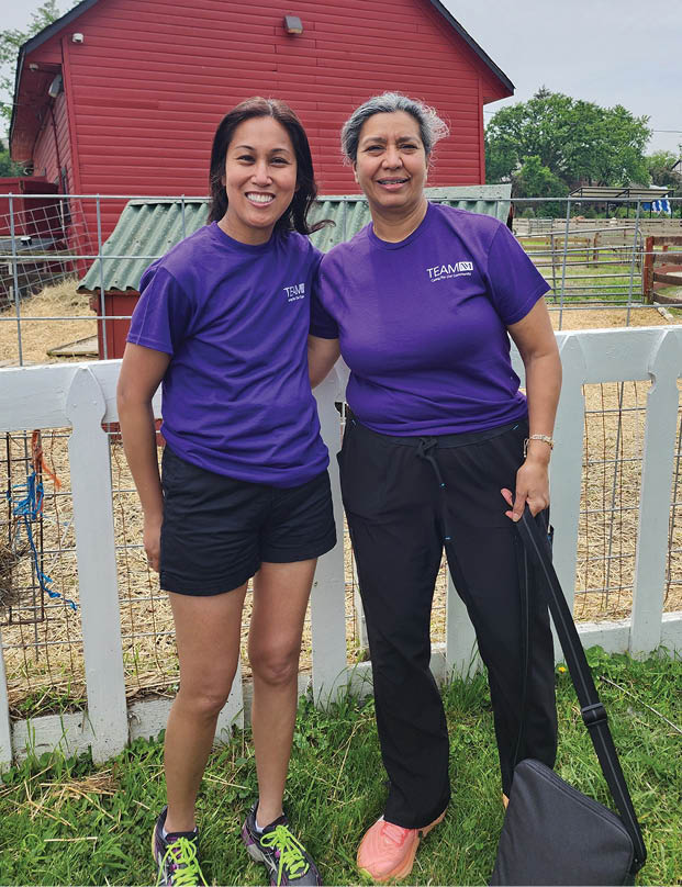 Two women standing in front of a red barn. Description generated by AI