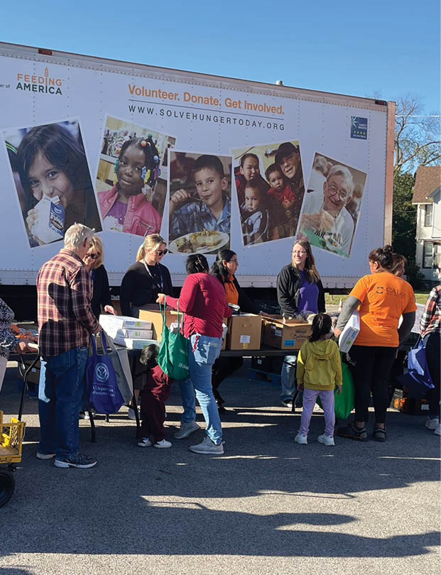 A large group of people are standing in front of a truck that says Northern Food Bank. Description generated by AI