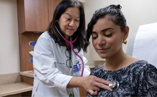 A woman wearing a white coat and a stethoscope is checking a woman's heart. Description generated by AI