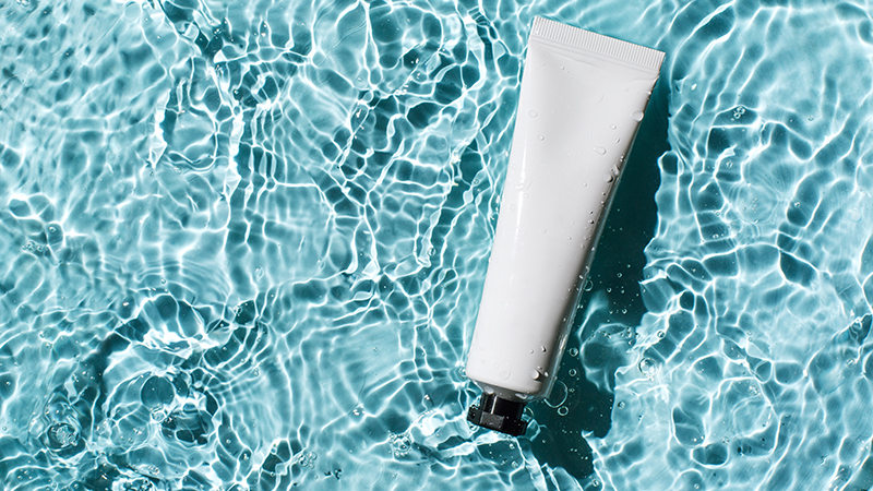 Tube of sunscreen floating in a light blue pool with rippled water.