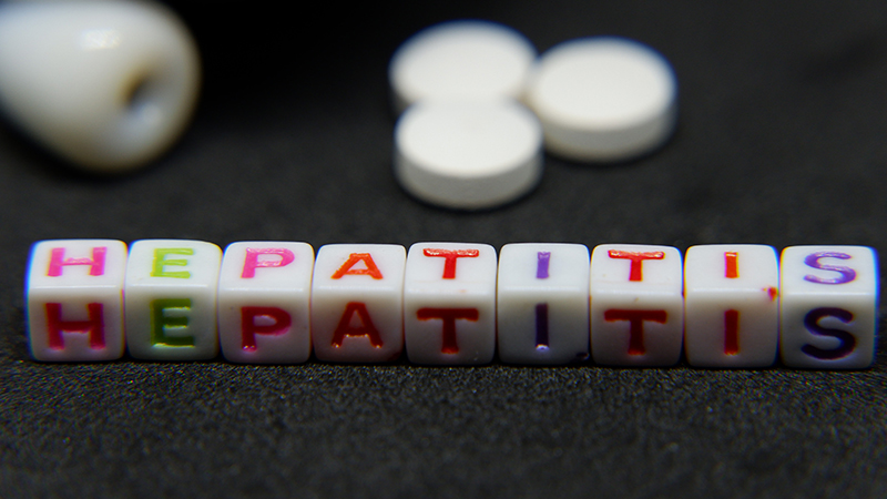Photo of white plastic block letters on a dark background spelling Hepatitis in pink, green, red and purple.