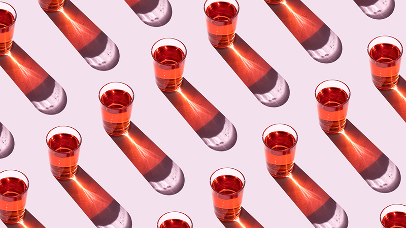 Repeating pattern of a photo of a red liquid in a shot glass on a light lavender background with bright light source from the upper left.