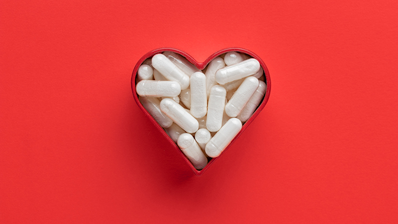 Heart-shaped container filled with white supplements on a red background.