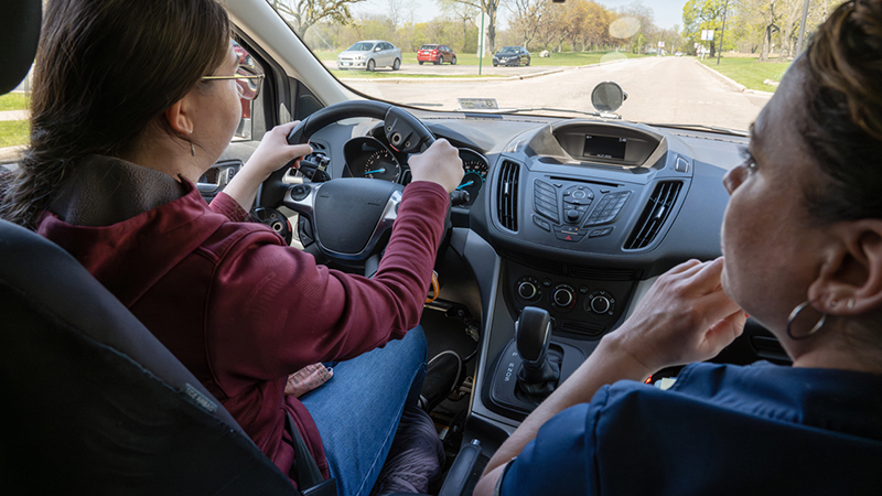 A driving instructor giving a lesson to a new driver in a vehicle.