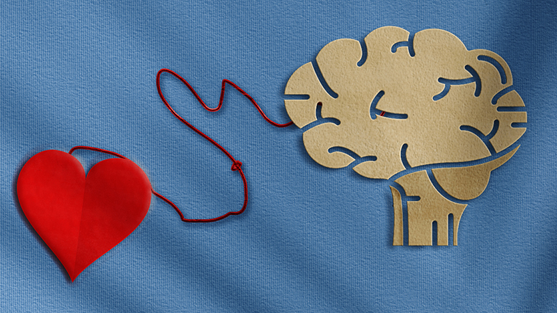 Overhead image of a heart shape, made out of fabric, attached by a red string to a cardboard cutout of a brain all over a light blue fabric background.