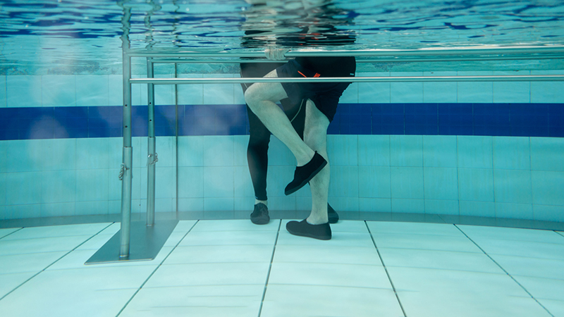 Underwater image of two people's legs in a pool participating in aquatic therapy.