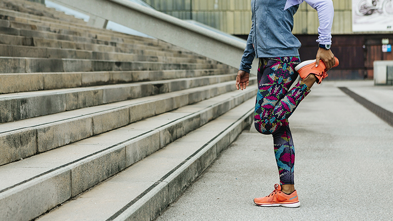 Person stands on one foot near steps doing a quad stretch outdoors