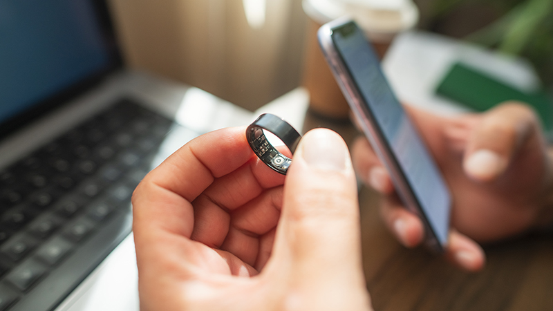 A person holding a smart ring and phone to track sleep.