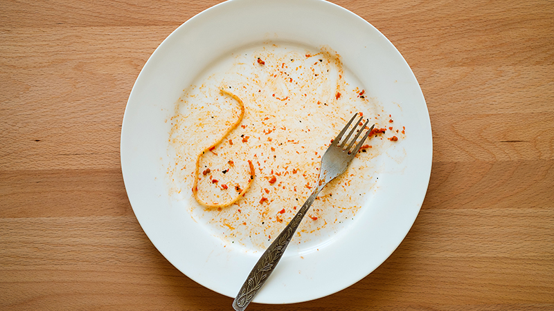 A dirty plate with one piece of pasta left behind.
