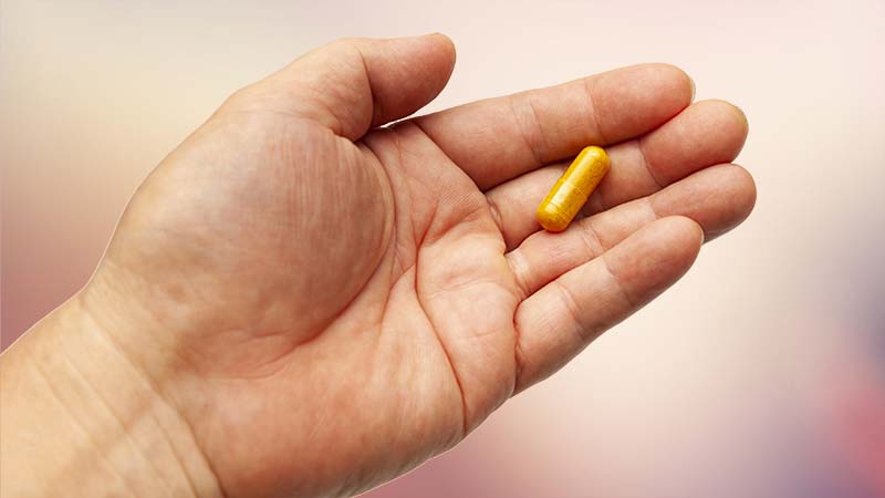 A hand holding a golden turmeric pill.
