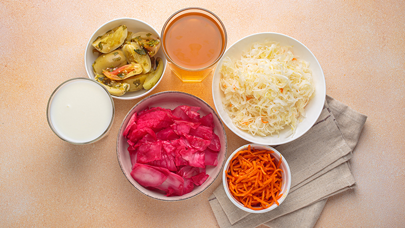 Six fermented foods, including pickled carrots, kefir and sauerkraut in bowls.