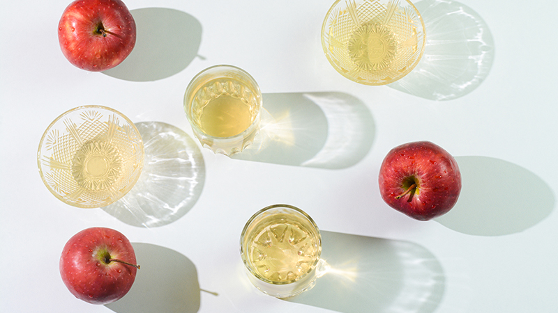 Apple cider vinegar and whole, red apples arranged on a light green table.