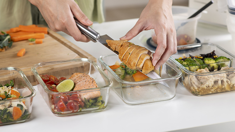 A person placing portions of a variety of foods into four separate clear containers on a counter.  