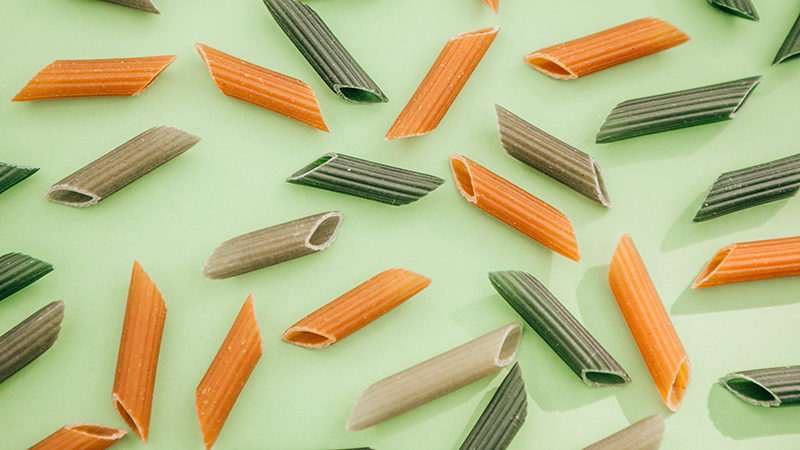 Green and orange penne pasta noodles arranged on a green background.