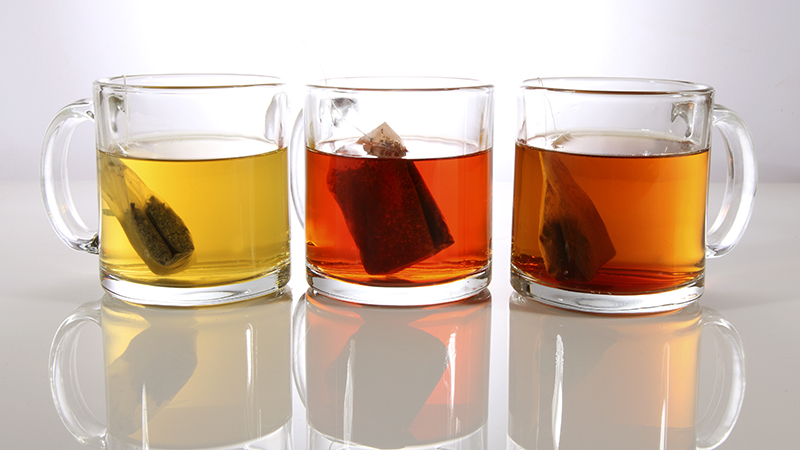 Three glass mugs of different types of tea on a table. 