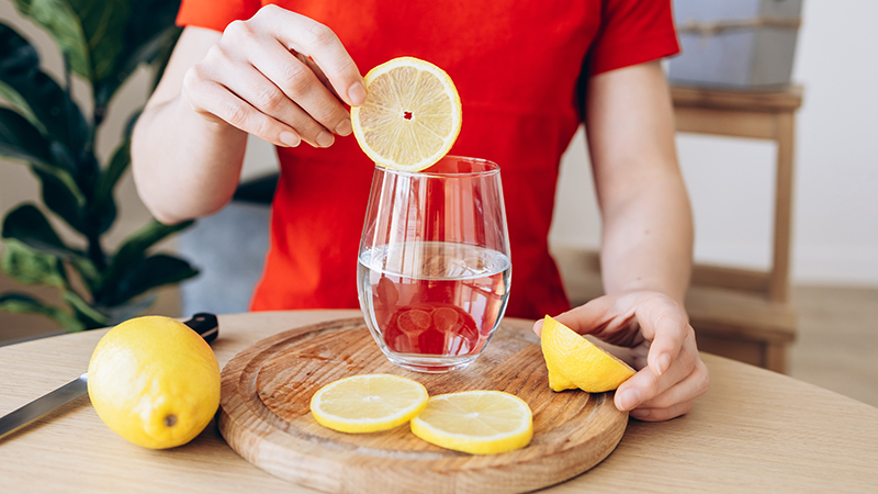 Person placing a slice of lemon into a glass water.