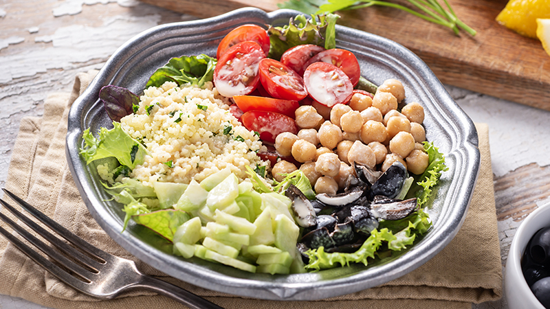 Salad, cucumbers, chickpeas, tomatoes, couscous, black olives, lemon and parsley representing the Mediterranean diet.