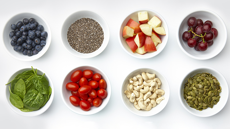 Bowls with blueberries, chia seeds, apples, red grapes, spinach, grape tomatoes, cashews and pepitas.