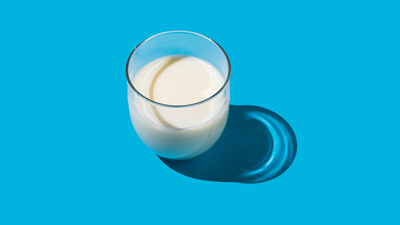Glass of milk in hard light on a blue background.