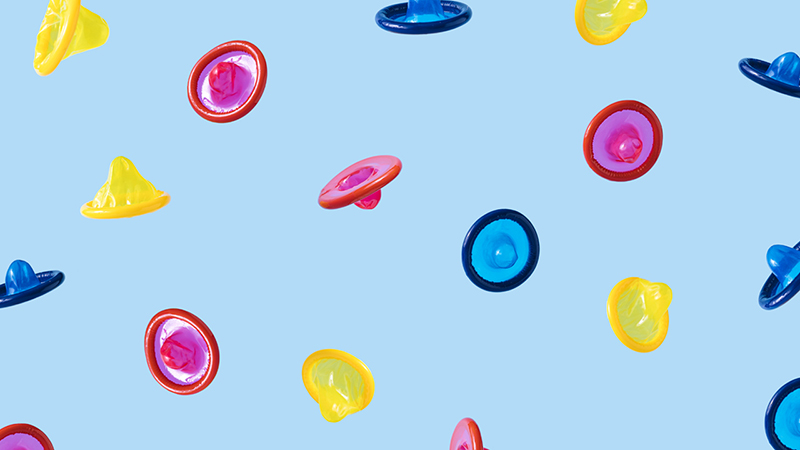 Pink, yellow, and blue condoms on a light blue background, as if falling through space.