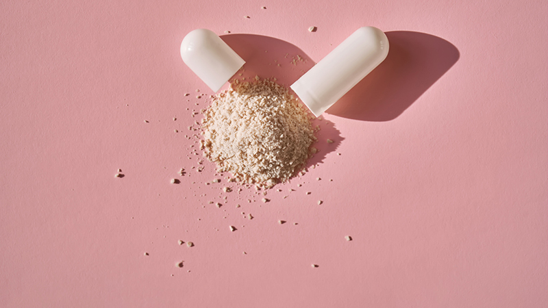 An open capsule with its contents on a pink background.