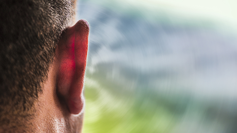 Closeup of a human ear with an outdoor background.