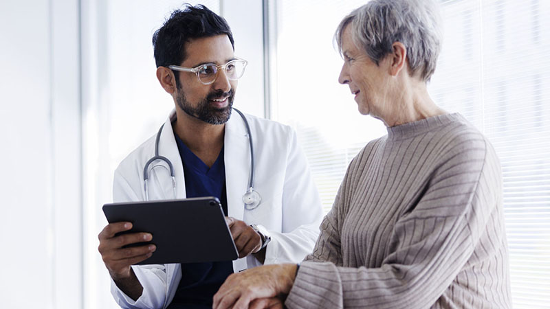 A physician speaking to a patient while both look over a tablet. 