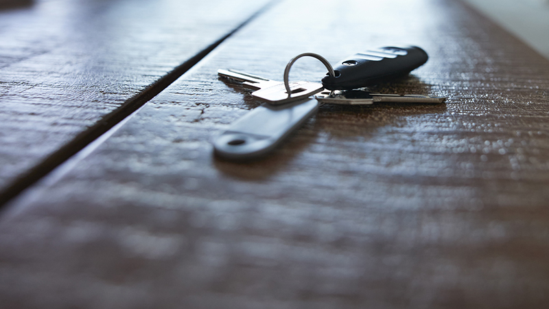 A keyring with keys and automobile key fob on a wooden table top.