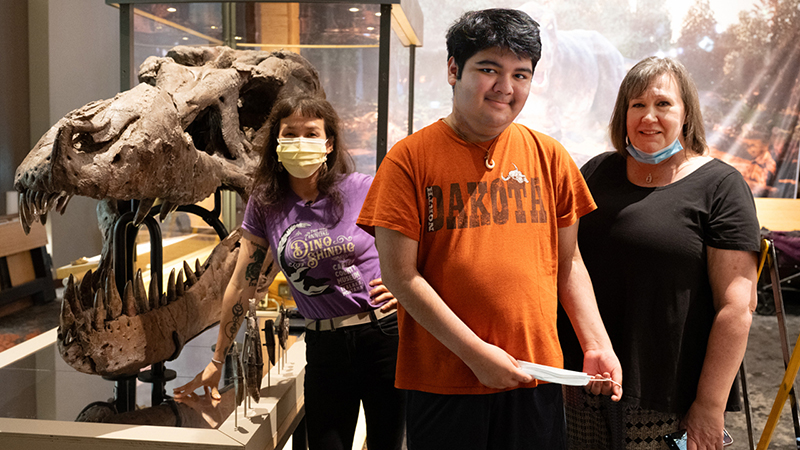 Jingmai Conner, PhD, of the Field Museum, Josh Burton and his mother Kelly Burton, standing next to a Tyrannosaurus rex skull.